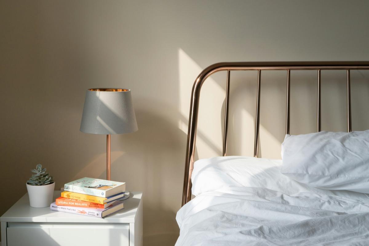 Table lamp with a gray shade and copper stand on a white nightstand beside a bed