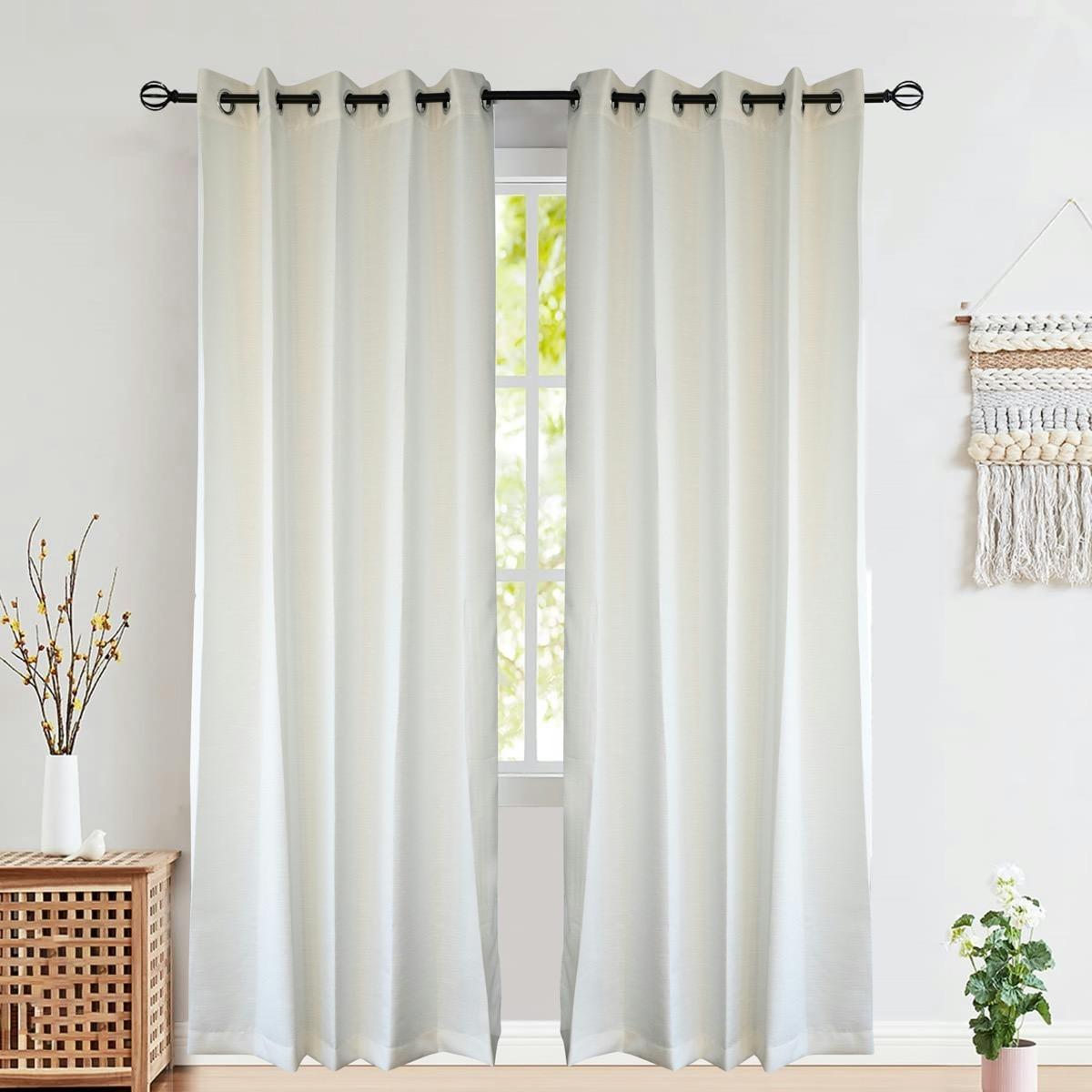 Cream grommet-top curtains hanging on a rod beside a bright bedroom window