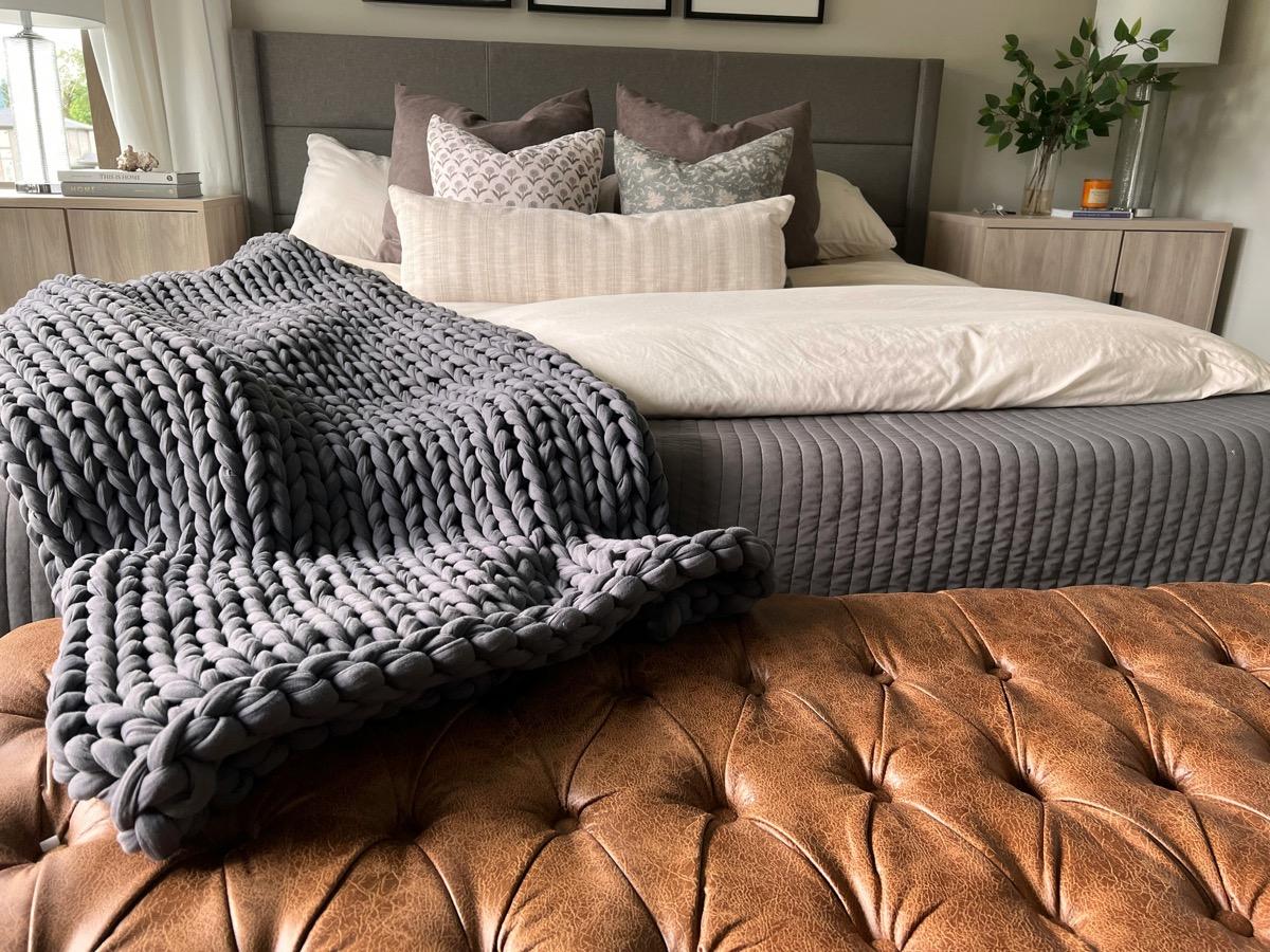 Grey chunky knit throw blanket draped over a leather bench at the foot of a bed