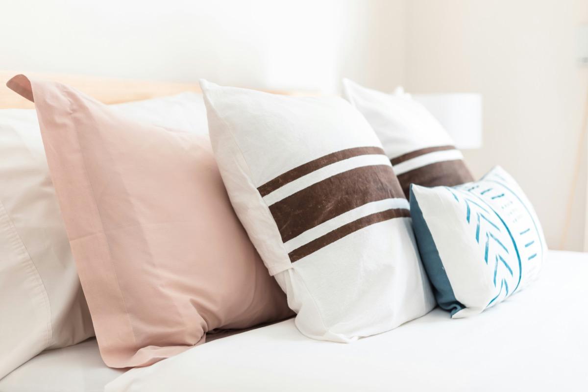 Blush pink, striped and patterned decorative cushions arranged on a white bed