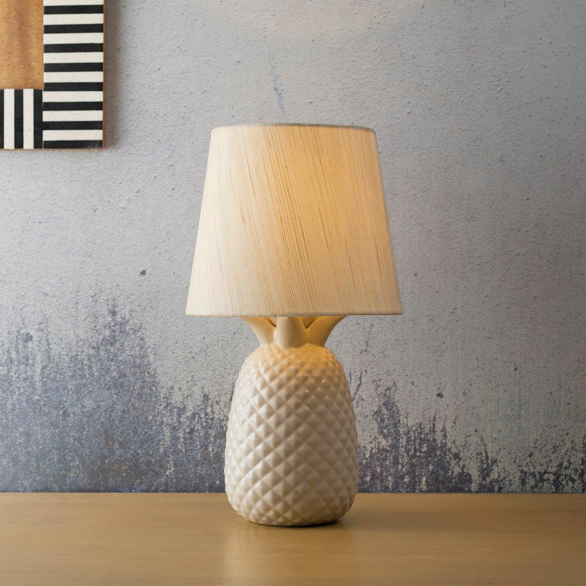 Cream ceramic table lamp with fabric shade lit warmly on a wood console