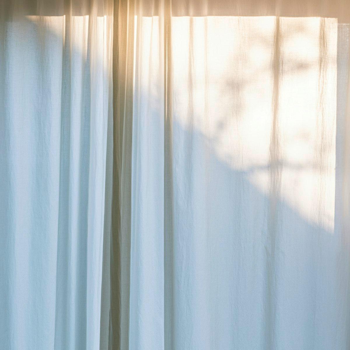 Sheer white linen curtains diffusing warm window light