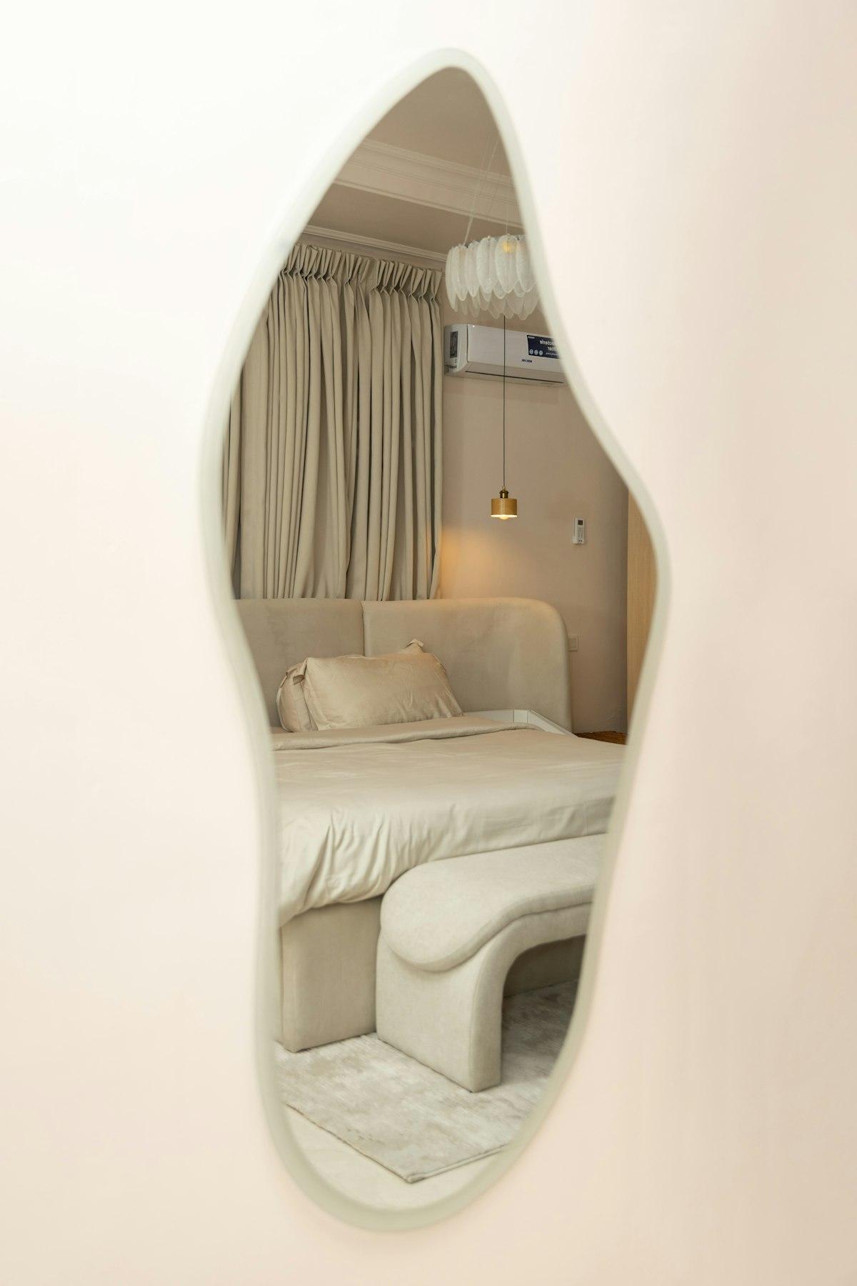 Mirror with an irregular organic shape reflecting a bedroom