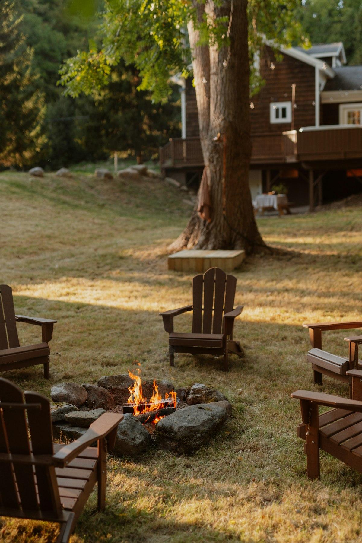 Stone-ringed garden fire pit with flames surrounded by Adirondack chairs at golden hour