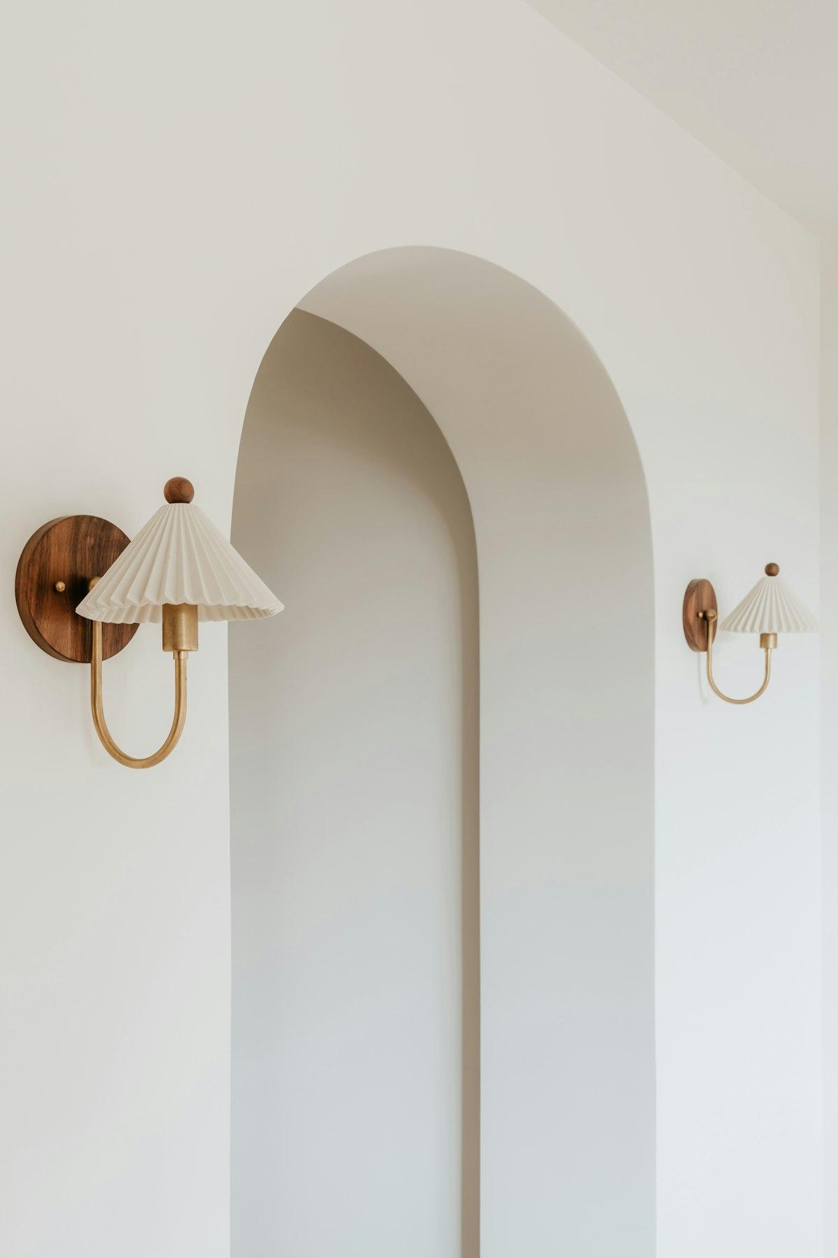 Brass and wood wall sconces with pleated shades on a white arched wall