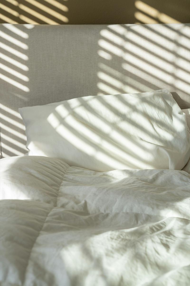 Soft white washed-linen duvet and pillow with warm sunlight stripes across the bed