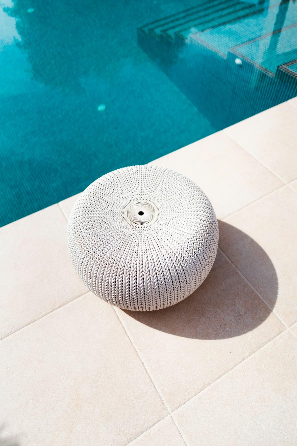 White knitted-resin outdoor pouf beside a swimming pool