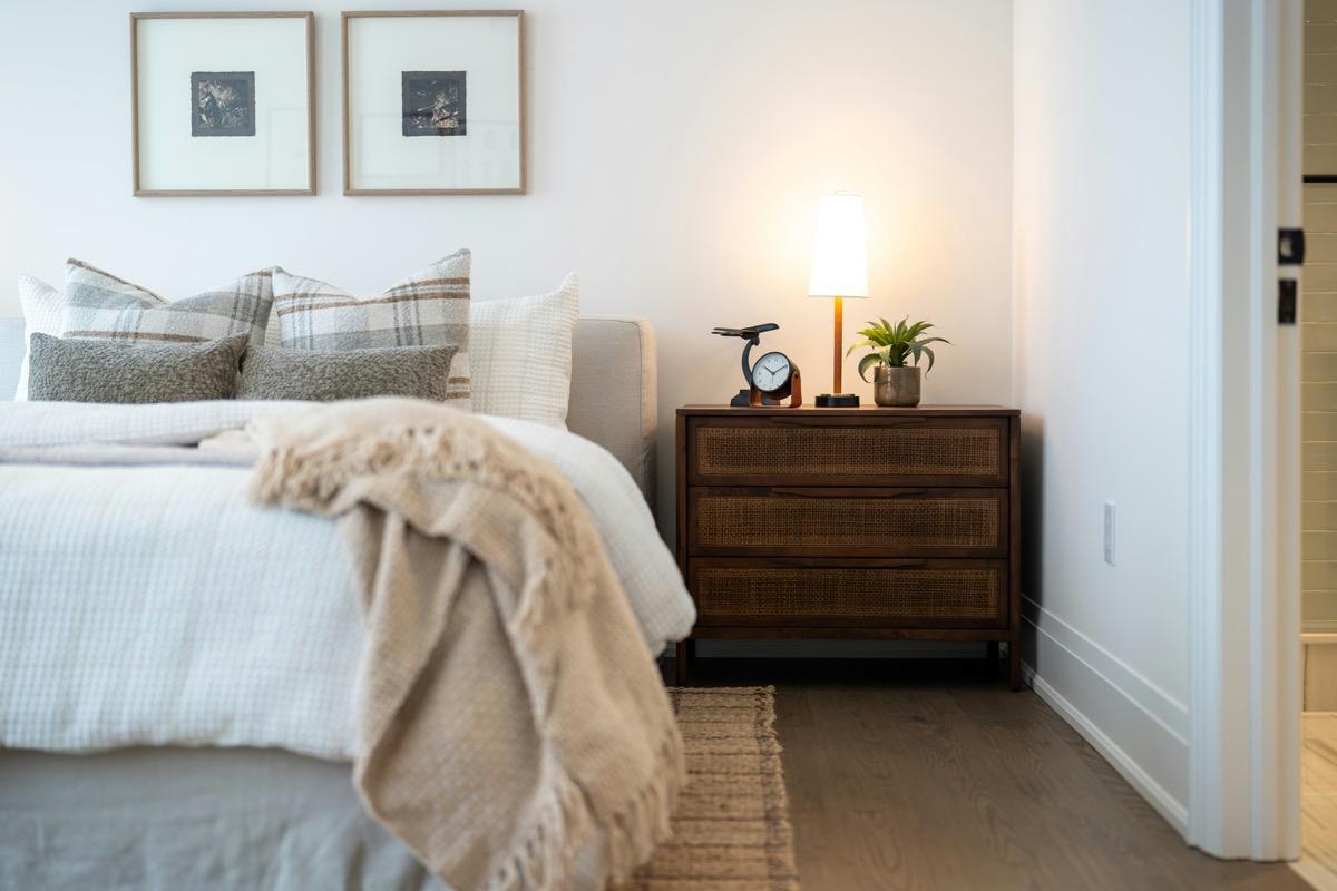 Woven neutral rug on the floor beside a bed next to a lit lamp and nightstand